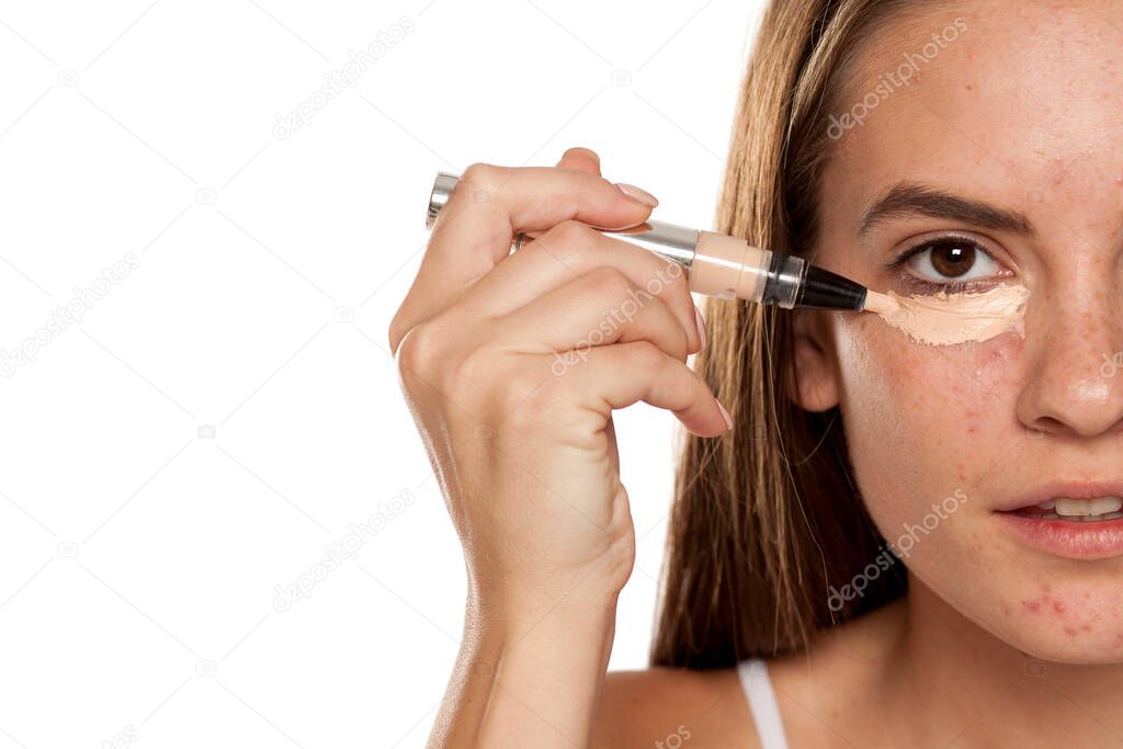 young beautiful girl applying concealer under her eyes on white backgeound