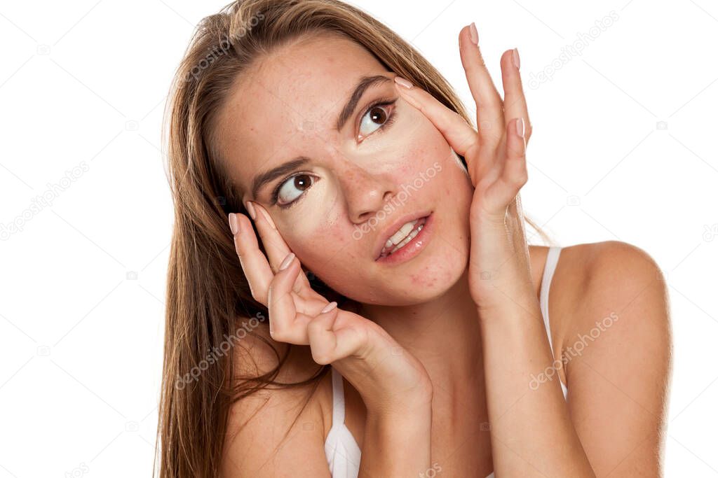 young beautiful girl applying concealer with the fingers under her eyes on white backgeound