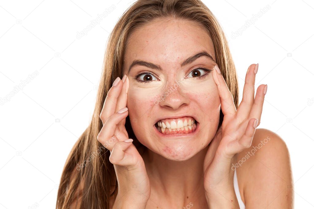 young funny girl applying concealer with fingers under her eyes on white backgeound
