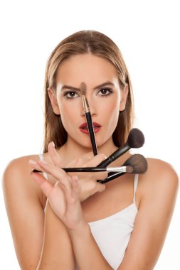 Beyaz arka planda makyaj fırçalarıyla poz veren güzel bir kız.