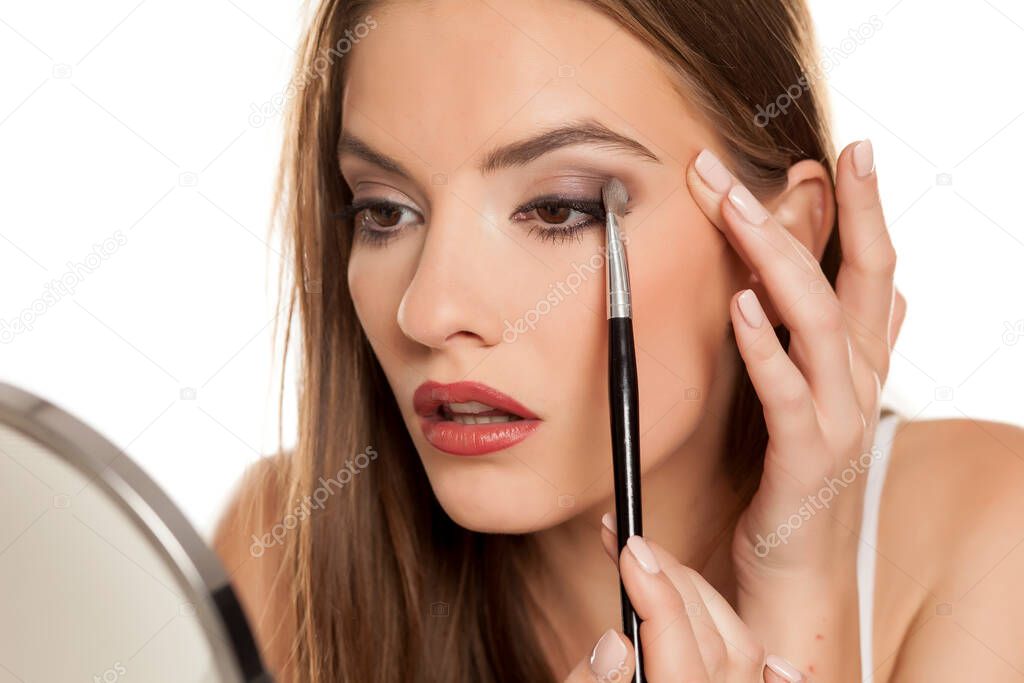 young beautiful girl apllying eyeshadow with makeup brushe on white backgeound