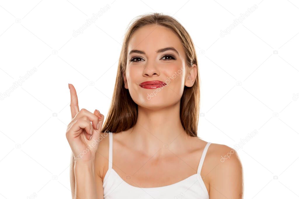 Portrait of young beautiful happy woman pointing up on white background