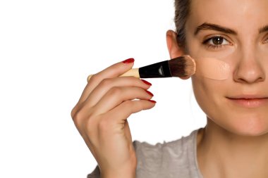 Beyaz arka plana sıvı temel uygulayan genç bir kadın.