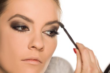 Beyaz arka planda kaşlarını fırçalayan genç bir kadın.