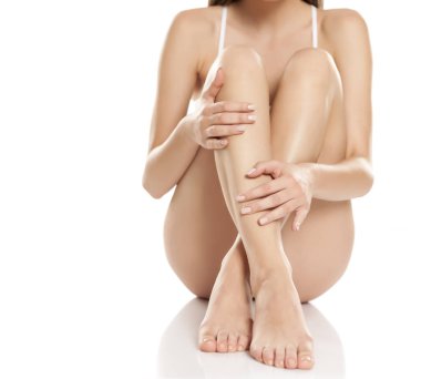 Kadın beyaz arka planda bacaklarına nazikçe dokunuyor.