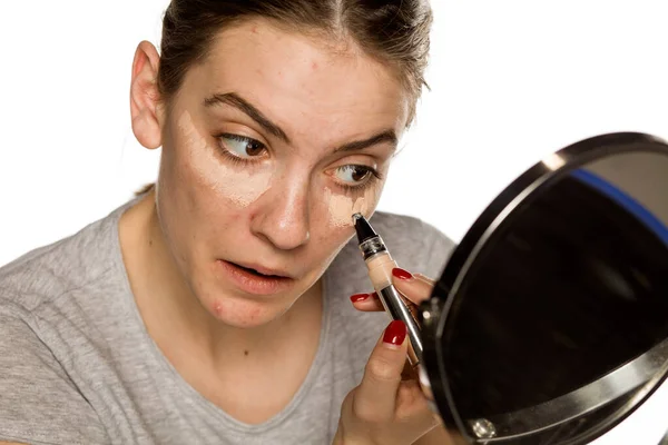 Mujer Joven Aplicando Corrector Sobre Fondo Blanco —  Fotos de Stock