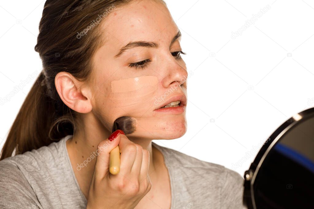 Young woman applying liquid foundation on white background