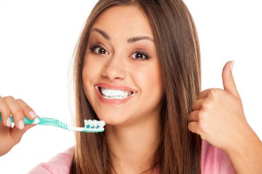 Beyaz arka planda diş fırçası tutan ve baş parmağını gösteren genç bir kadın.