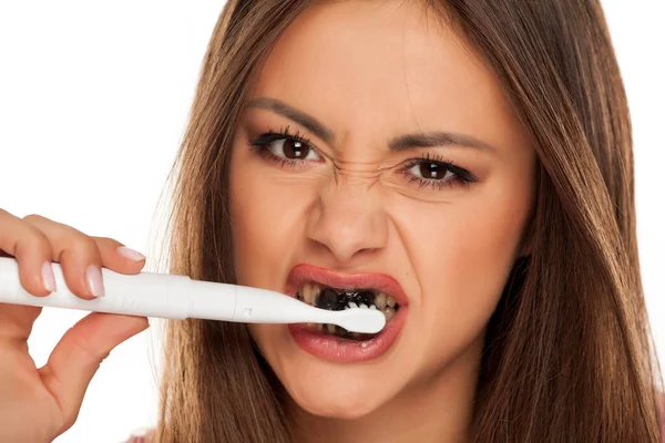 歯を電動歯ブラシでブラッシングする若い女性白地に黒い活性炭の歯磨き粉で — ストック写真