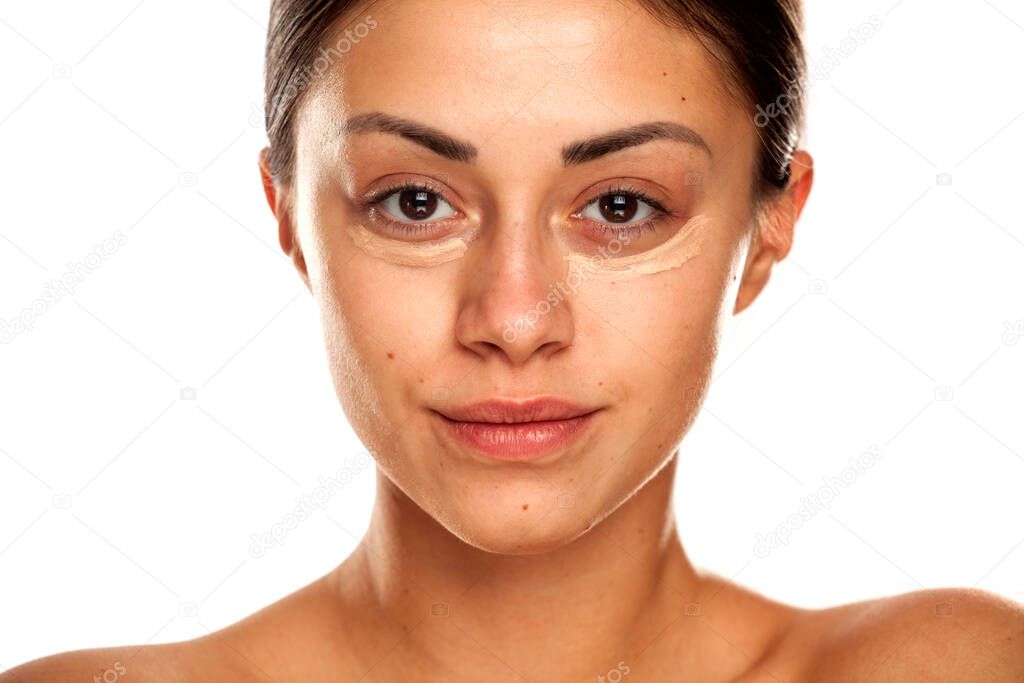 young beautiful girl posing with concealer under her eyes on white background