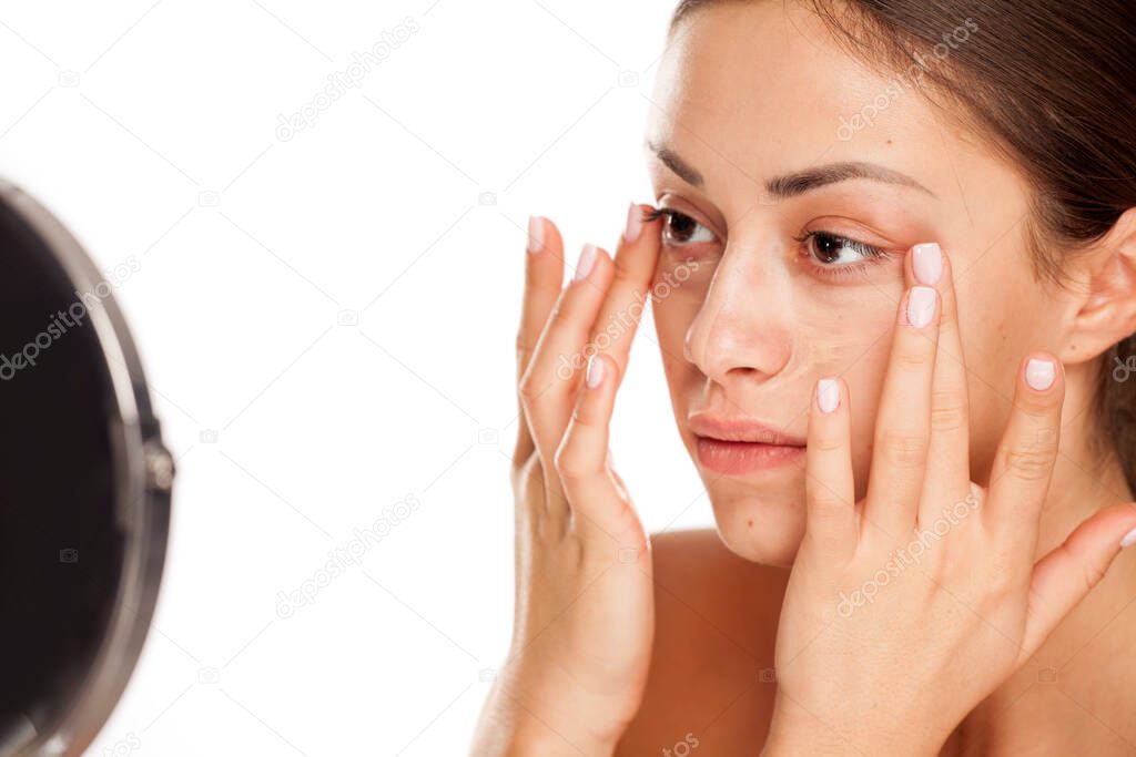 young beautiful girl applying concealer with fingers under her eyes on white background