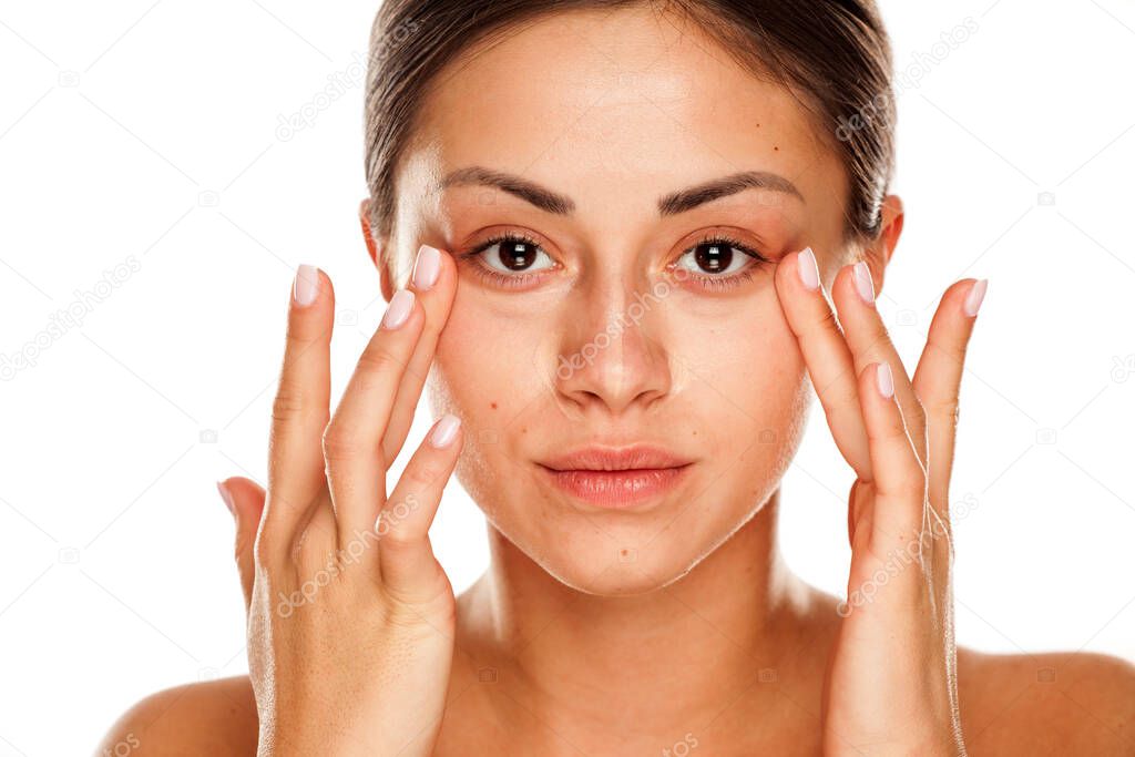 young beautiful girl applying concealer with fingers under her eyes on white background