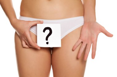 Woman in panties cowers her vagina with question mark drawn on sheet of paper on white background