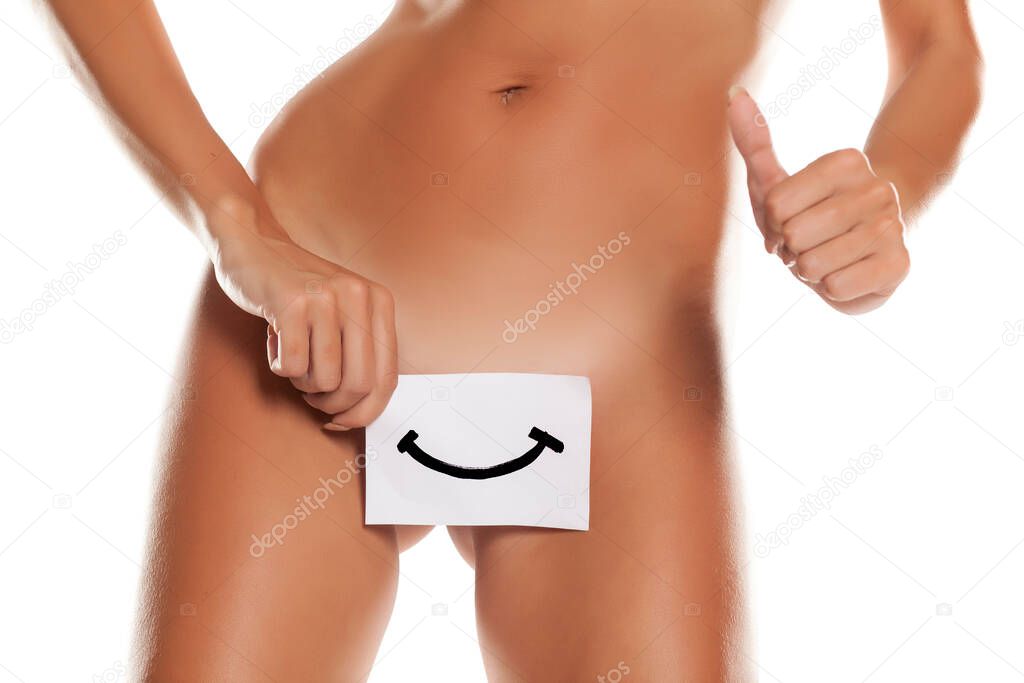 Nude woman cowers her vagina with smile drawn on sheet of paper on white background and showing thumbs up