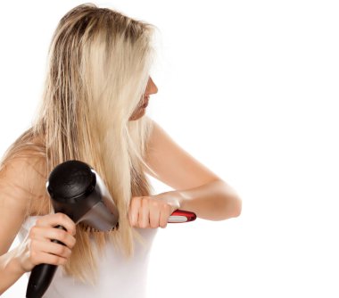 Bilinmeyen genç bir kadın saçını kurutma makinesiyle beyaz arka bahçede kurutuyor.