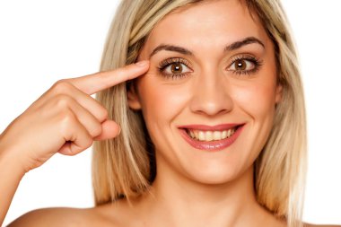 Beyaz arka plandaki göz kırışıklıklarına dokunan genç sarışın kadın portresi.