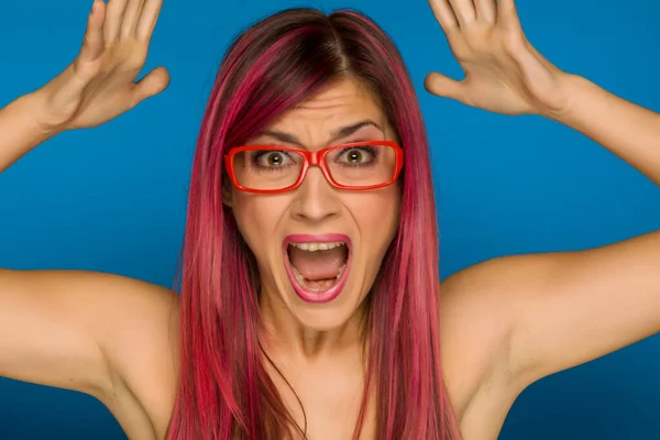 Young shocked woman with pink hair on blue background