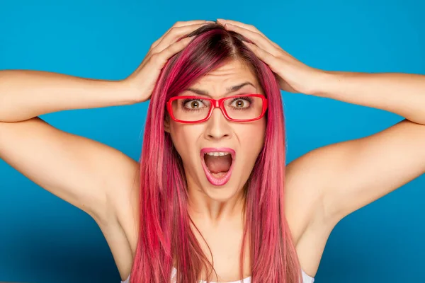ショックを受けた女性とともにピンクの髪と眼鏡で青の背景 — ストック写真