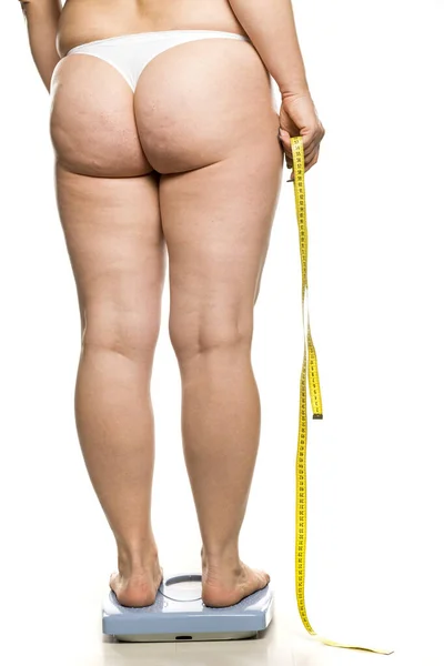 太った女性がうろこの上に立って白い背景に測定テープを持っていて — ストック写真