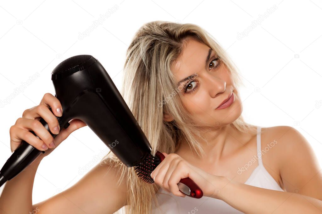 smiling young woman drying her hair with hair dryer on white backgrund