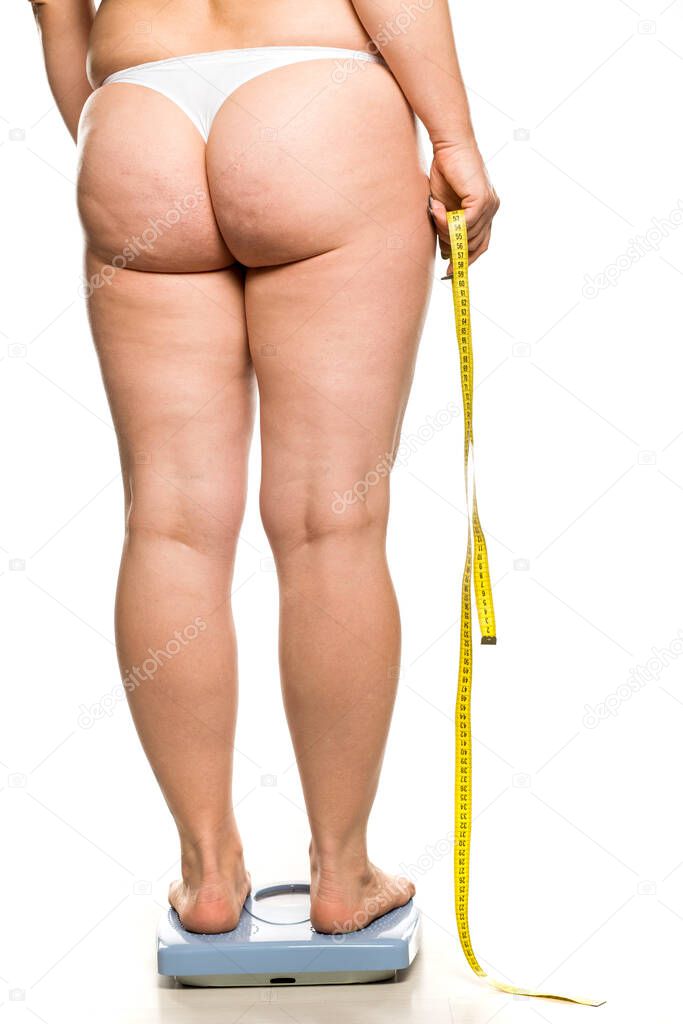 a fat woman stands on a scales and holds a measuring tape on white background