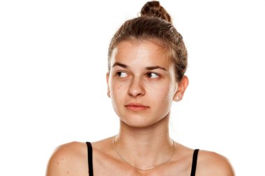 Beyaz arka planda makyajsız genç, ciddi bir kadın, yana bakıyor.