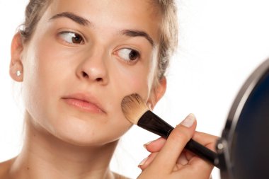 Beyaz arka planda fırçayla sıvı temel uygulayan genç bir kadın.