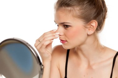 Genç bir kadın beyaz arka planda burnuna dokunuyor.