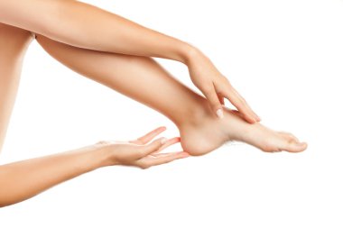 Genç bir kadın beyaz arka planda bacaklarına krem sürüyor.