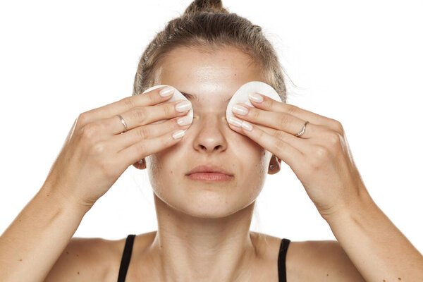 Young woman cleaning her makeup with cotton pads on white background