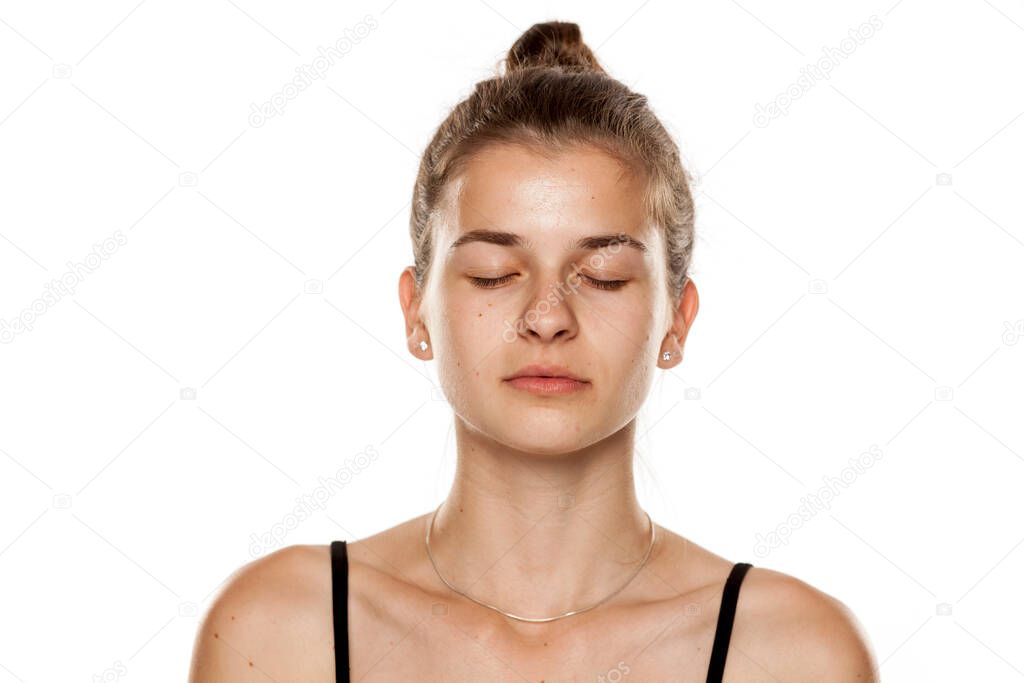 Young serious woman without makeup and with closed eyes on white background
