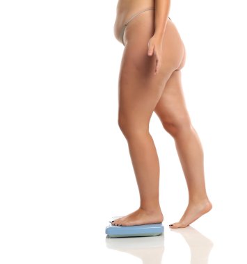 Beyaz arka planda ağırlık ölçeğinde duran büyük beden kadın bacaklarının stüdyo görüntüsü