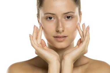 Stüdyoda makyajsız genç bir kadının beyaz arka planda nazikçe gülümsemesi.