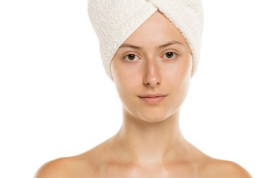 Beyaz arka plana sarılmış havluyla genç bir kadının stüdyo fotoğrafı.