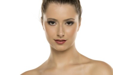 Kahverengi saçlı, makyajlı ve beyaz arka planda hafifçe gülümseyen genç bir kadının stüdyo fotoğrafı.