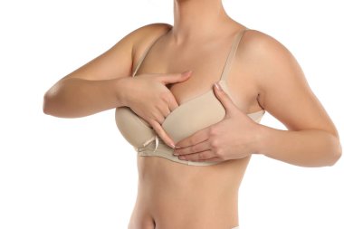 Bej renkli sutyen giymiş, göğüslerini muayene eden, beyaz arka planda göğüsleri olan bir kadının stüdyo fotoğrafı.