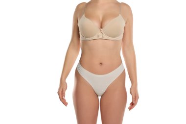 Bej sutyen ve külot giymiş beyaz arka planda poz veren genç bir kadının gövdesi.