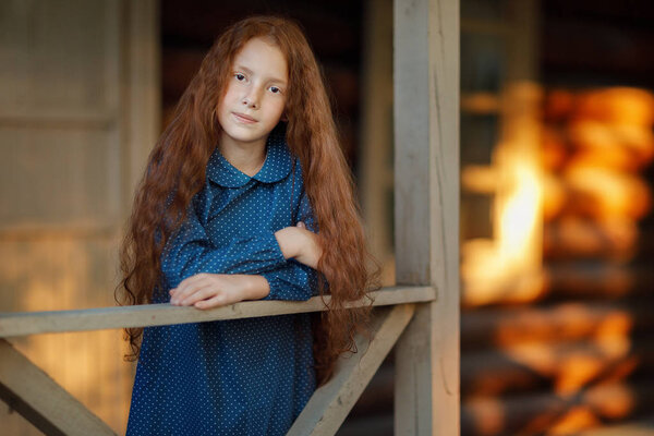 cheerful red haired girl standing on the porch and looking at the camera 