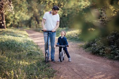 Babası kickscooter ve oğlu birbirine Park yolundaki bakarak bisiklet sürme 