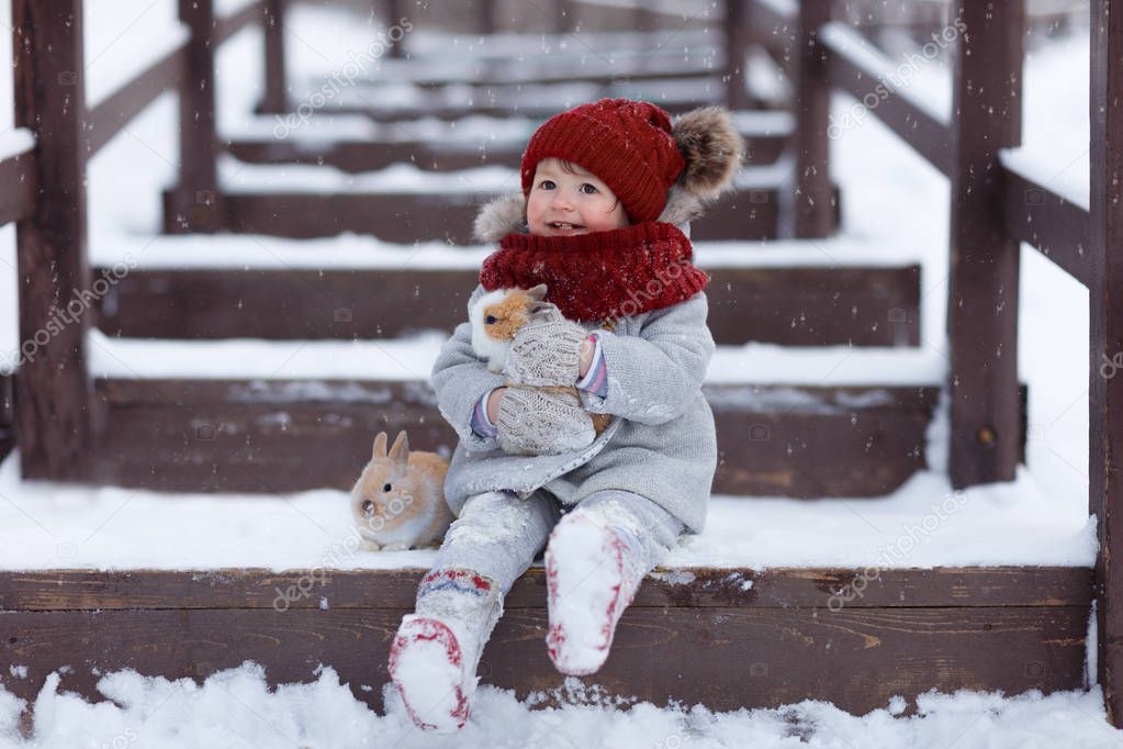 cheerful girl sitting on the steps on wooden bridge  with rabbits in the park at winter 