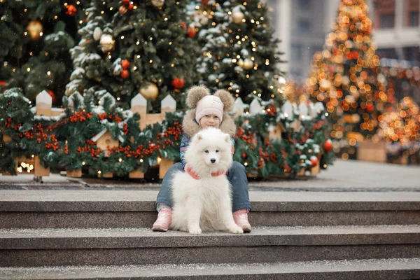 girl with dog sitting on the stairs with christmas trees on the background