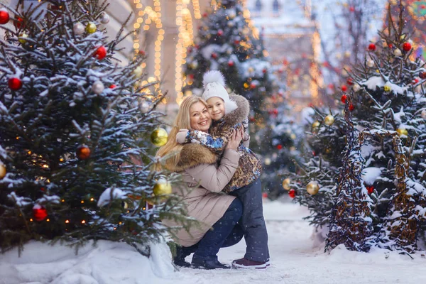 gülümseyen anne ve kızı kameraya sokakta Noel ağaçları ile arıyorum.