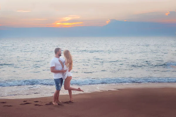 full length of man and woman standing in the ocean at sunset