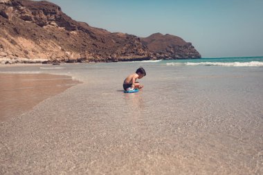  Sahilde oturan ve oyuncak tekne ile oynayan bir çocuk