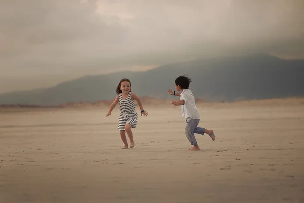 two children running and playing in catch up on the beach together