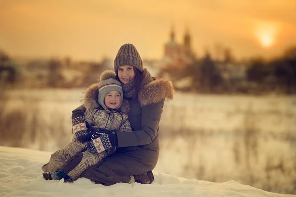 mother hugging son sitting on her the laps outdoors in winter at the sunset