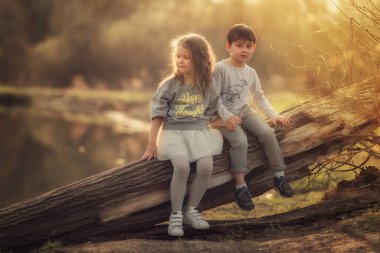 bahar parkında kütük üzerinde oturan ve el ele tutuşan çocuklar 