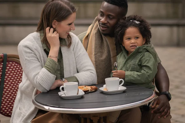 father, mother and daughter sitting in outdoor cafe drinking coffee