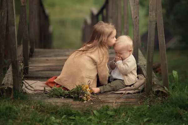 sister kissing in the head her younger brother on the wooden bridge