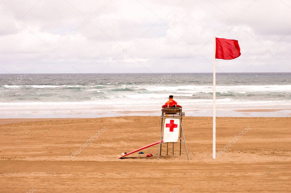 A lifeguard sitting in his chair, front of the sea, at the end of summer.